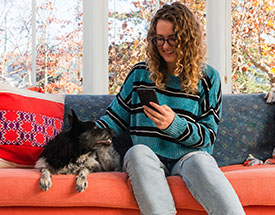 Girl sitting on a couch looking at her smartphone while sitting next to a dog